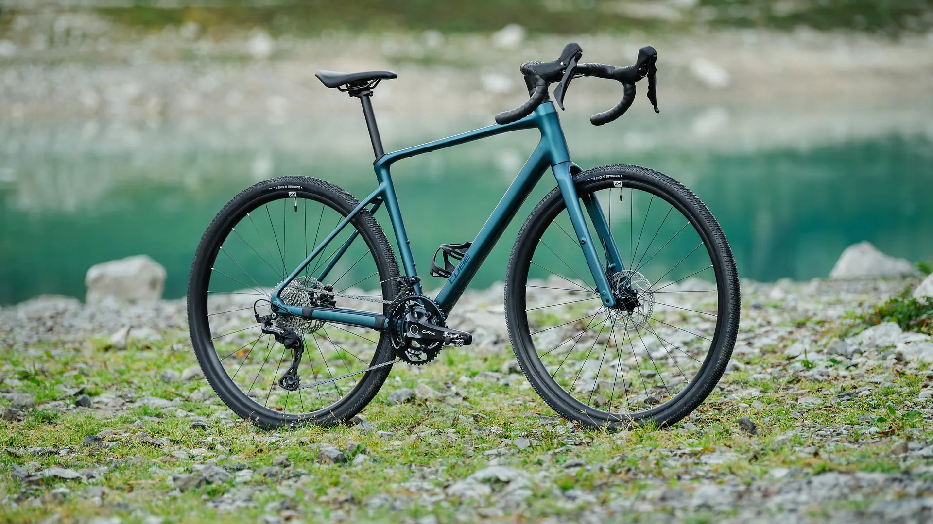 Grünes Cube Nuroad Race auf einem steinigen Pfad vor einem See, ideal für Offroad-Abenteuer und Outdoor-Enthusiasten.