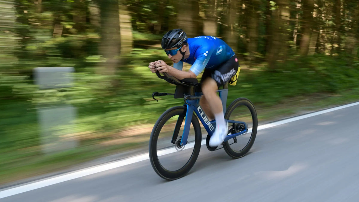 Radfahrer auf Cube Aerium in Aktion, schneller Sprint auf einer Straße durch bewaldete Landschaft.